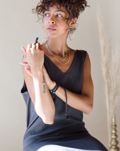 Model, Natalia, wearing the Charcoal romp around reversible dress. The model is sitting, with the braided belt around their wrist. Size M shown. 